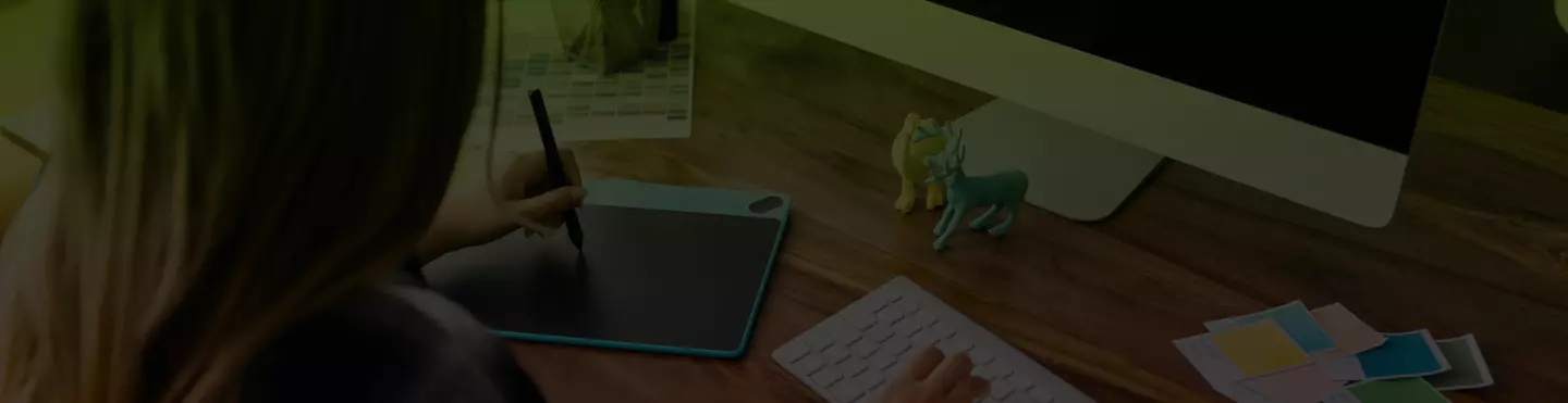 kobieta siedząca przy biurku rysująca na tablecie graficznym